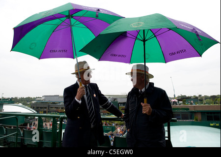 Verwalter halten Sonnenschirme im Regen während der 2011 Wimbledon Tennis Championships Stockfoto