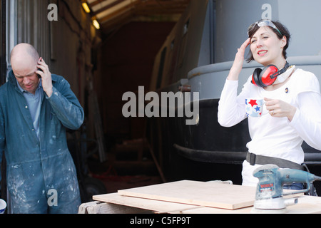 Mann und Frau eine Pause von Arbeiten für den Bau eines Bootes, eine Tasse Tee trinken und am Telefon zu sprechen. Stockfoto