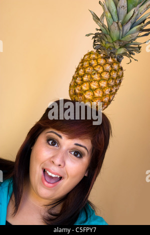 Eine junge Frau mit einem lustigen Ausdruck eine Ananas auf dem Kopf balancieren. Stockfoto