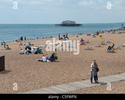 Brighton Strand-Szene mit Sonnenanbeter auf Liegestühlen und dem zerstörten West Pier im Hintergrund Stockfoto