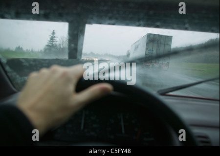 Eine Ego-Perspektive des Fahrens in einem Auto neben einem LKW-Anhänger an einem regnerischen Tag indem man unter einer Straßenüberführung. Stockfoto