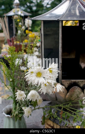 Blumen, Laternen und andere Objekte bilden eine Outdoor-Altar-Display in einem buddhistischen Tempel in Nordthailand. Stockfoto