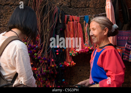 Ein ausländischer Tourist spricht mit einer ethnischen Hügel Stamm Frau tragen traditionelle Kleidung auf einem Straßenmarkt in Nordthailand. Stockfoto