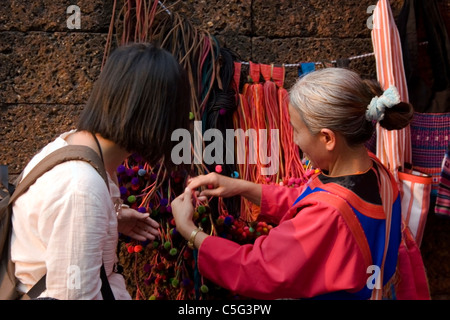 Ein ausländischer Tourist spricht mit einer ethnischen Hügel Stamm Frau tragen traditionelle Kleidung auf einem Straßenmarkt in Nordthailand. Stockfoto