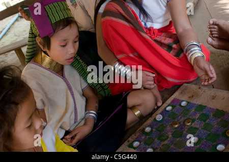 Eine Karen Paduang Flüchtling Mädchen tragen goldene Ringe um den Hals spielt Dame mit Freunden in einem Flüchtlingslager in Thailand. Stockfoto