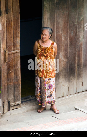 Eine ältere Frau blickt auf eine Straße von der Tür ihres Hauses in kommunistische Laos. Stockfoto