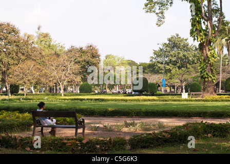 Junge Frau sitzt auf einer Bank in Unabhängigkeit Palastgärten, Siem Reap, Kambodscha Stockfoto