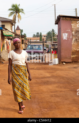 Afrikanische Frau im Kopftuch, die auf einer staubigen Stadtstraße läuft, Accra, Ghana Stockfoto