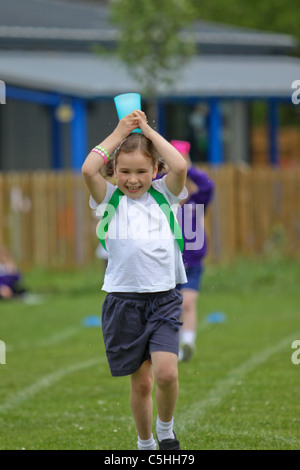 Junges Mädchen in einem Laufwettbewerb mit Tasse Wasser auf Kopf während sportsday Stockfoto