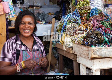Lächelnde Schmuckhändlerin am farbenfrohen Halskettenstand in Makola Market, Accra, Ghana Stockfoto