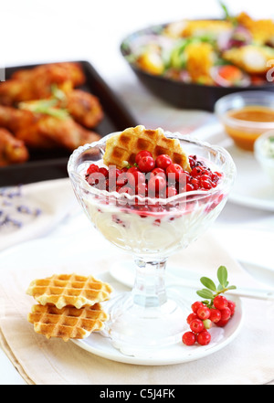 Joghurt mit karamellisierten Früchten mit Chicken Wings und Gemüsesalat im Hintergrund Stockfoto