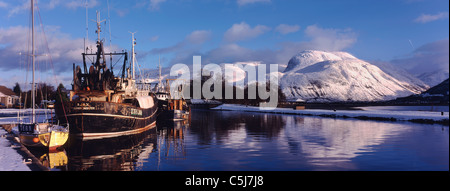 Fischerboote liegen im westlichen Becken des Caledonian Canal auf einem knackigen Wintertag mit voller Schnee und blauer Himmel. Ben Stockfoto