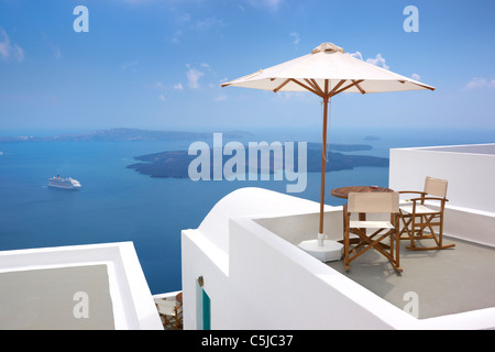 Thira (Hauptstadt von Santorini) - Terrasse mit Liegestühlen, Sonnenschirm und blauen Meer im Hintergrund, Insel Santorin, Griechenland Stockfoto