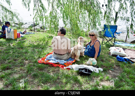 mittleren Alter Brautpaar mit Hund genießen schattige Plätzchen auf dem Rasen am Gewässerrand an einem heißen Sommertag im Riverside Park in New York City Stockfoto