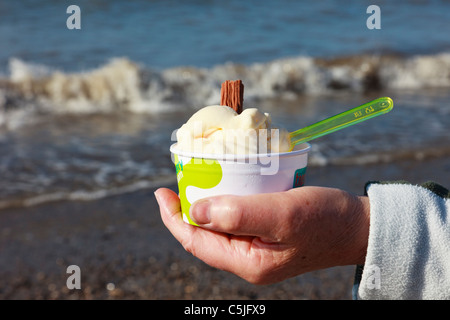 Frau Hand mit einer Wanne mit Eis mit Schokolade Flocken am Strand. UK, Großbritannien. Stockfoto
