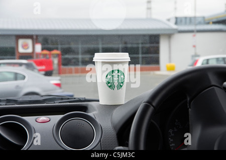Starbucks-Kaffee in einem Pappbecher zum mitnehmen auf dem Armaturenbrett eines Autos in einer Autobahn-Tankstelle gehen. England, UK Stockfoto