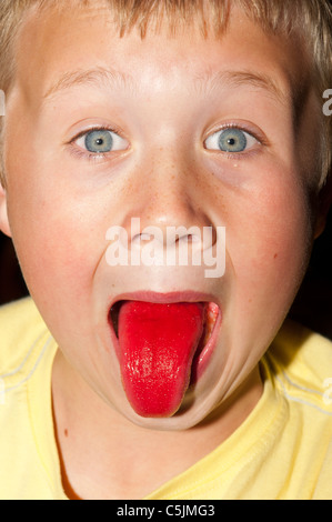 Ein sieben Jahre alter Junge zeigt seine rote Zunge nach dem Trinken eines Drink Erdbeer Slush puppy Stockfoto