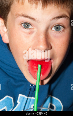 Ein elfjähriger Junge zeigt seine rote Zunge nach dem Trinken eines Drink Erdbeer Slush puppy Stockfoto