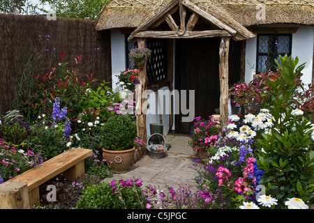 Blumengarten Sitzbank im Reetdachhaus mit grob behauenen Veranda Hölzern. 'The Cottage Tür' Zurück zu Garten auf der Rückseite eine Landschaft Garten Ausstellung RHS Royal Horticultural Show Tatton Park, Cheshire, Juli 2011. Stockfoto