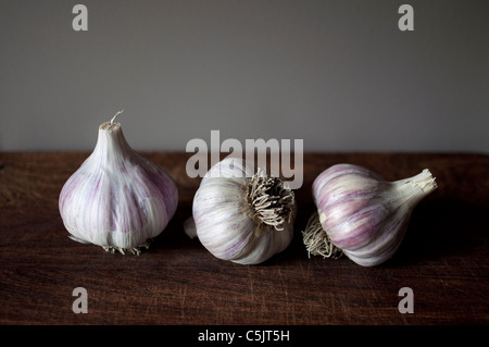 Drei Birnen mit lila Streifen (aka Chesnok rot) Knoblauch in einer Linie auf ein Schneidebrett. Stockfoto