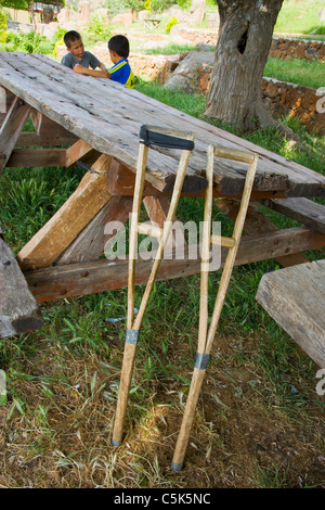 Ein paar alte Krücken lehnte sich gegen einen alten hölzernen Picknick-Tisch mit zwei lokalen Jungs im Hintergrund, Yesemek Dorf, Stockfoto