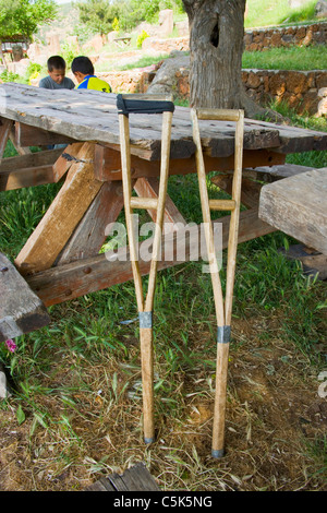 Ein paar alte Krücken lehnte sich gegen einen alten hölzernen Picknick-Tisch mit zwei lokalen Jungs im Hintergrund, Yesemek Dorf, Stockfoto