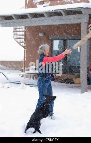 Vertikale Frau werfen Stick für Hund im Schnee Stockfoto