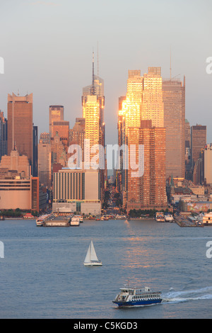 Die untergehende Sonne spiegelt sich in den Fenstern der Manhattan Wolkenkratzer auf der 42nd Street über den Hudson River von New Jersey aus gesehen Stockfoto