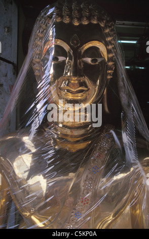 Große Messing Statue des Buddha verpackt in transparenten Polyethylen vor einem Geschäft in Bangkok, Thailand Stockfoto