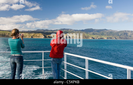 Zwei Passagiere (Rückansicht) auf eine Inter-Island-Fähre in Cook Strait, fotografieren die Ufer von Wellington Harbour und Stockfoto