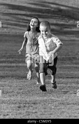 Einen kleinen Jungen und Mädchen Lachen und laufen durch die Wiese in schwarz und weiß. Stockfoto