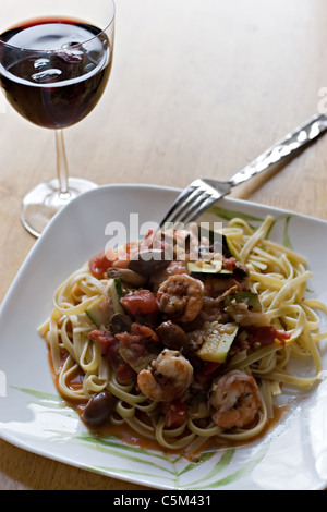 Eine leckere Garnelen und Pasta Gericht zusammen mit einem Glas Rotwein. Stockfoto
