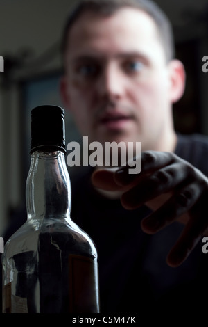 Ein Mann kämpft mit Alkoholismus greift nach seiner Flasche Schnaps. Geringe Schärfentiefe. Stockfoto