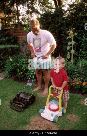 Vater mit Sohn spielt mit Spielzeug Mäher Rasen mähen Stockfoto