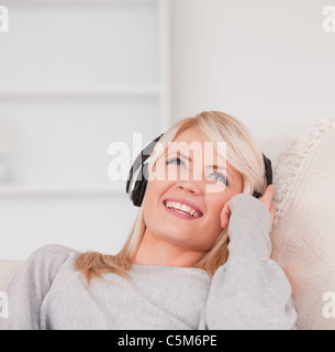 Hübsche junge blonde Frau mit Kopfhörern in einem Sofa liegend Stockfoto
