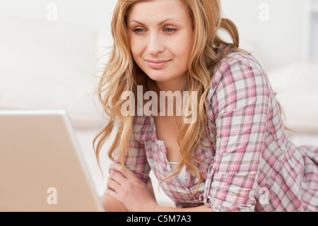 Süße Frau, die arbeitet auf ihrem Laptop auf dem Boden liegend Stockfoto
