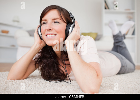 Fröhliche Brünette Frau mit Kopfhörern liegend auf einem Teppich Stockfoto
