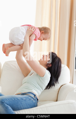 Wunderschöne Frau, die ihr Baby im Arm halten, beim Sitzen auf einem sofa Stockfoto