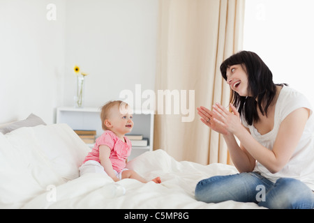 Wunderschöne Brünette Frau spielt mit ihrem Baby sitzend auf einem Bett Stockfoto