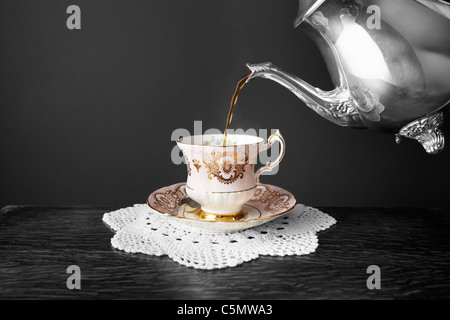 Gießen frisch gebraut Tee aus eine silberne Teekanne in einem Vintage fine Bone China Teetasse. Stockfoto