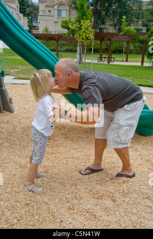 Ein liebevoller Vater küsst seine Tochter beim Spielen mit ihr in einem Park in Lake Forest, CA. Stockfoto