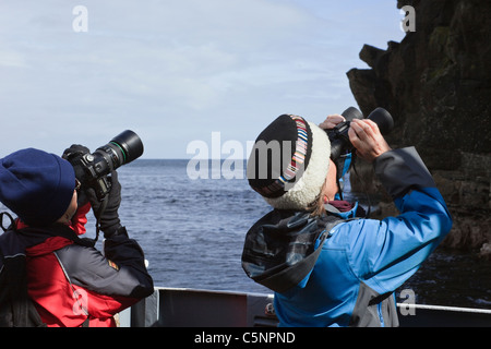 Zwei Frauen Vogelbeobachtung auf einen Bootsausflug zu den Basstölpel nisten auf den Seacliffs im Sommer. Noss, Shetland Islands, Schottland, Großbritannien. Stockfoto