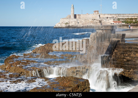 Kuba, Havanna. Wellen brechen sich am Malecon Sea Front. El Morro im Hintergrund Fort. Stockfoto