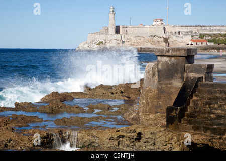 Kuba, Havanna. Wellen brechen sich am Malecon Sea Front. El Morro im Hintergrund Fort. Stockfoto