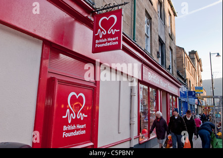 Geschäftige Hauptstraße am Markttag (Menschen, die Einkaufstaschen, Geschäfte und das Logo des britischen Herzstiftungsladens tragen - Otley, West Yorkshire, England. Stockfoto