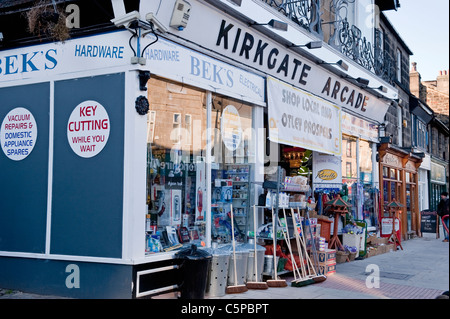 Kirkgate Arcade Eingang, Hardware Shop außen, Waren auf Straßenpflaster und in Fenster (Metallbehälter, Besen) - Otley, Yorkshire, England, Großbritannien. Stockfoto