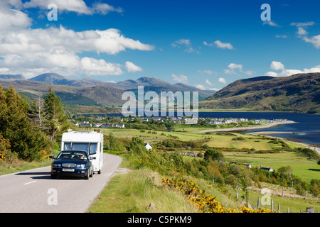 Auto und Wohnwagen auf der der A835 Hauptstraße mit Blick über Ullapool und Loch Broom, Ross und Cromarty, Highland, Schottland, Vereinigtes Königreich Stockfoto