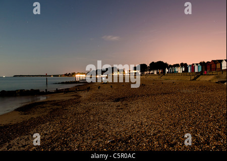 Strandhütten sind sichtbar gegen einen schwach beleuchteten Nachthimmel auf einem Kiesstrand in der Nähe von zuvorkommend, Dorset. Stockfoto