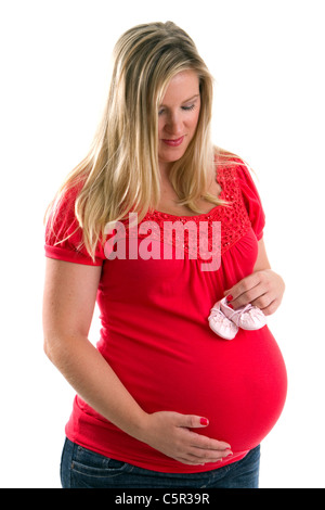 Nachdenkliche schwangere Frau hält Babyschuhe über ihre geschwollenen Bauch. Stockfoto