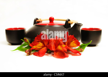 schwarzer Tee und Tassen mit Blumen auf weißem Hintergrund Stockfoto